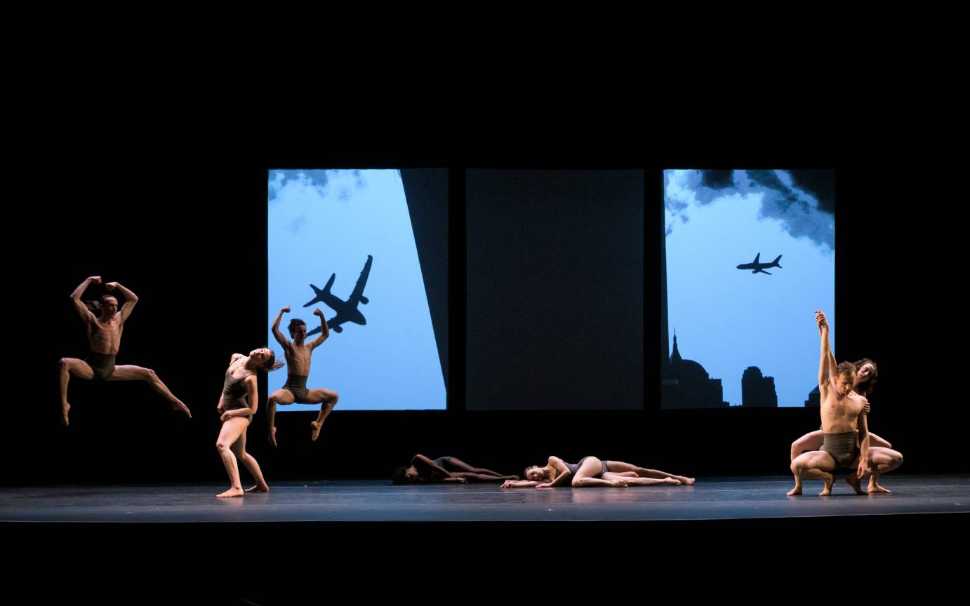 Dancers form a dynamic stage-scape in front of an image of planes in New York